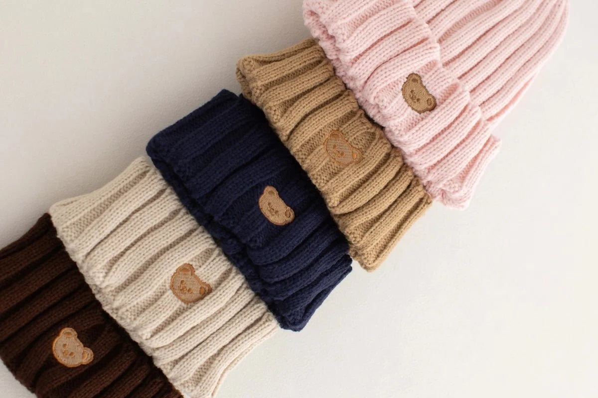 Set of knitted hats in various colors with bear emblem on a light background
