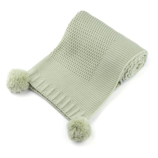 Green knitted blanket with pom-poms on a white background