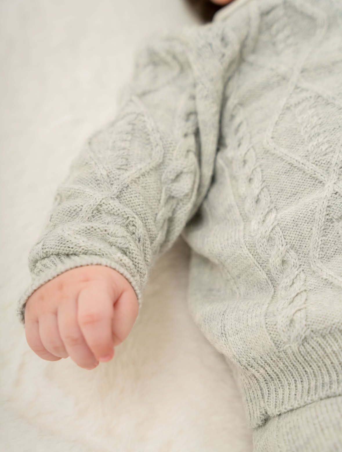 Close-up of a child's hand wearing a textured gray sweater on a light background