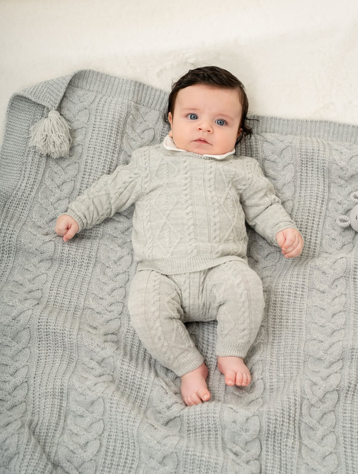 Baby in a gray outfit lying on a textured blanket