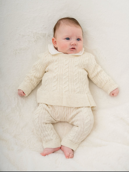 Baby in a cream knitted outfit lying on a white blanket