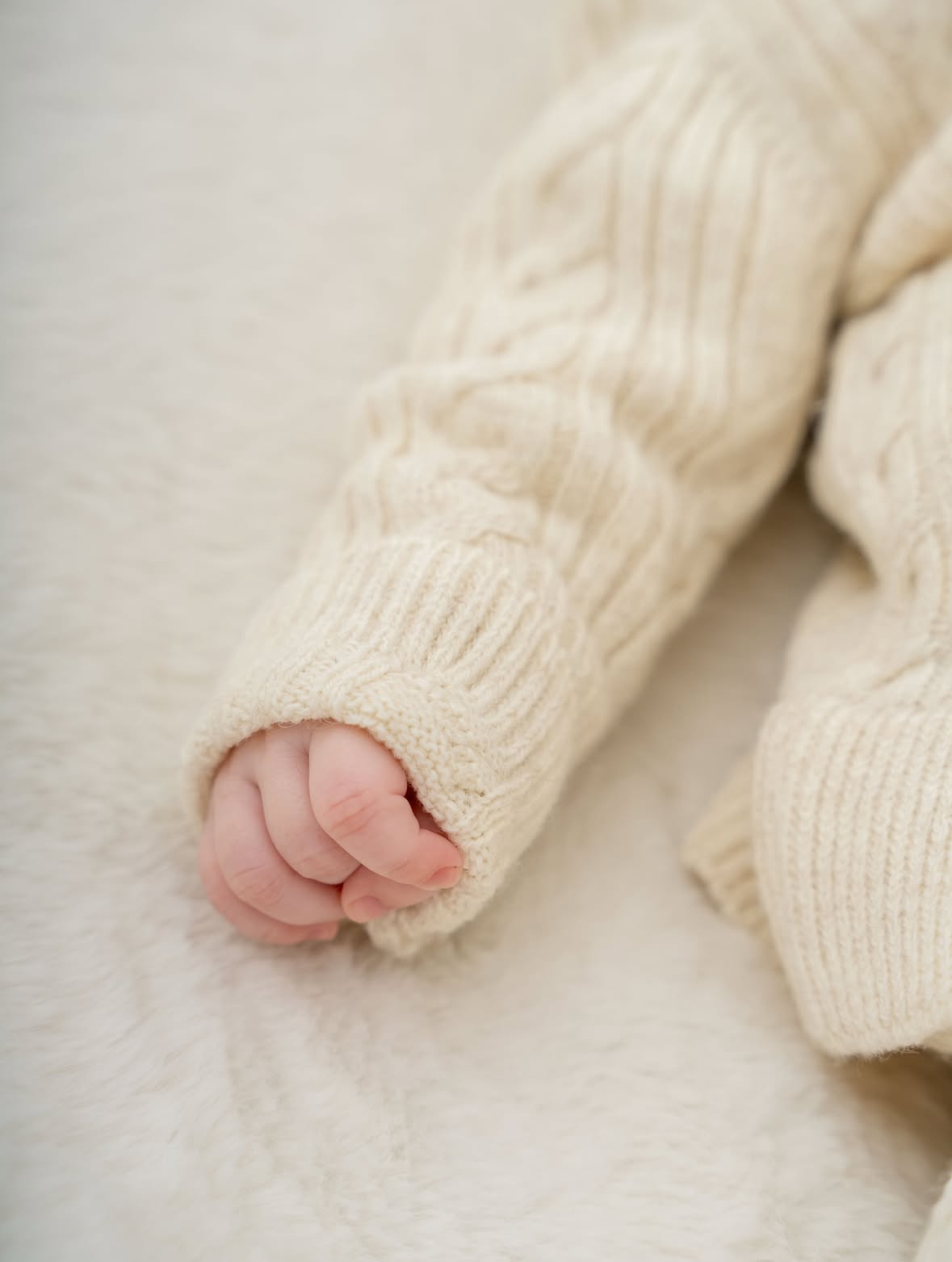 Close-up of a baby's hand in a cream-colored sweater on a soft surface